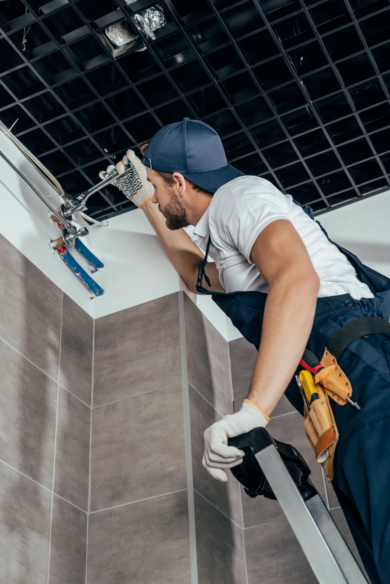 low angle view of plumber standing on ladder and working with pipes in bathroom