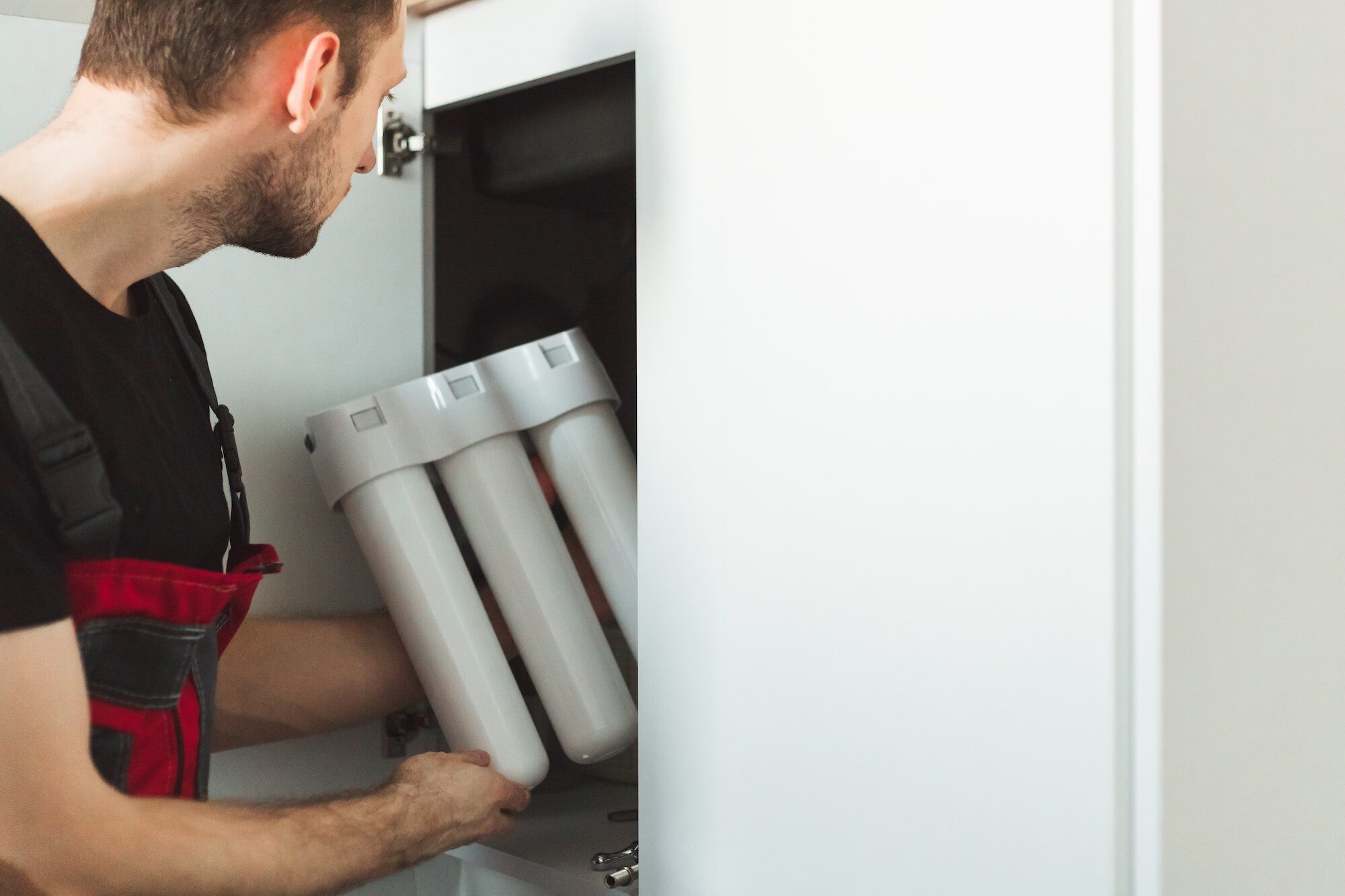 Plumber in the kitchen installs a household water treatment system. Three stage flask system